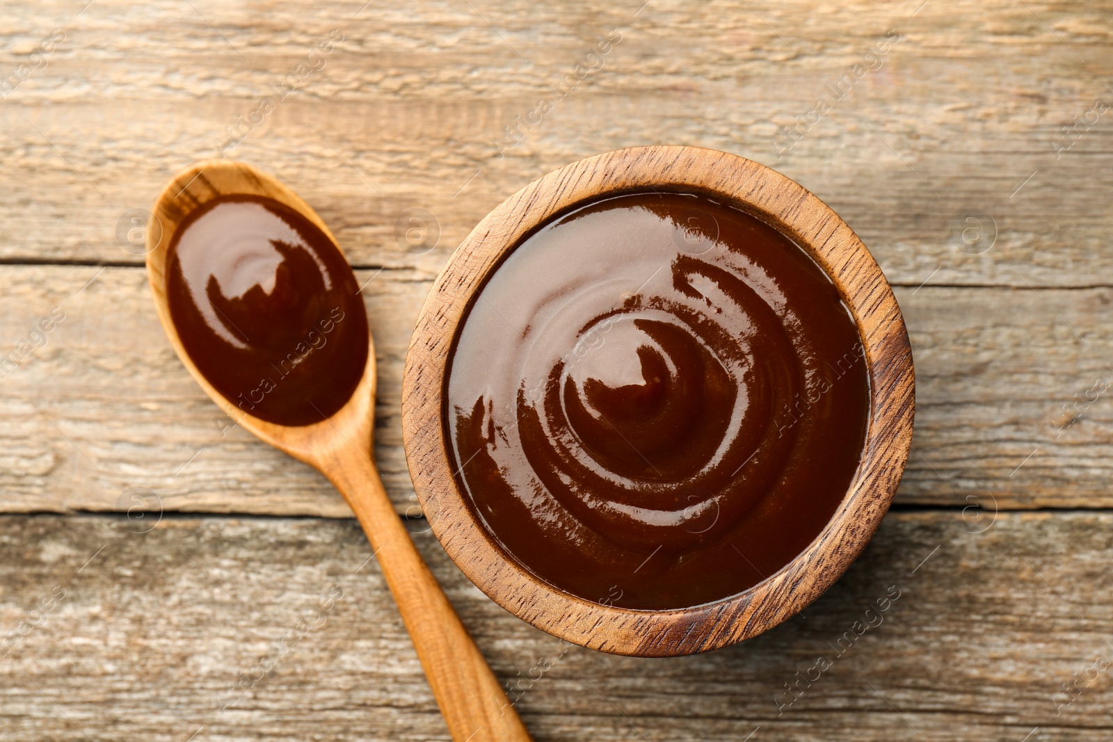 Photo of Tasty barbeque sauce in bowl and spoon on wooden table, top view