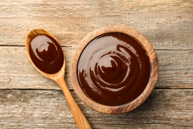 Photo of Tasty barbeque sauce in bowl and spoon on wooden table, top view