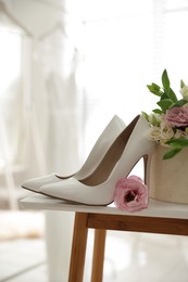 Photo of Pair of white high heel shoes, flowers and blurred wedding dress on background, space for text