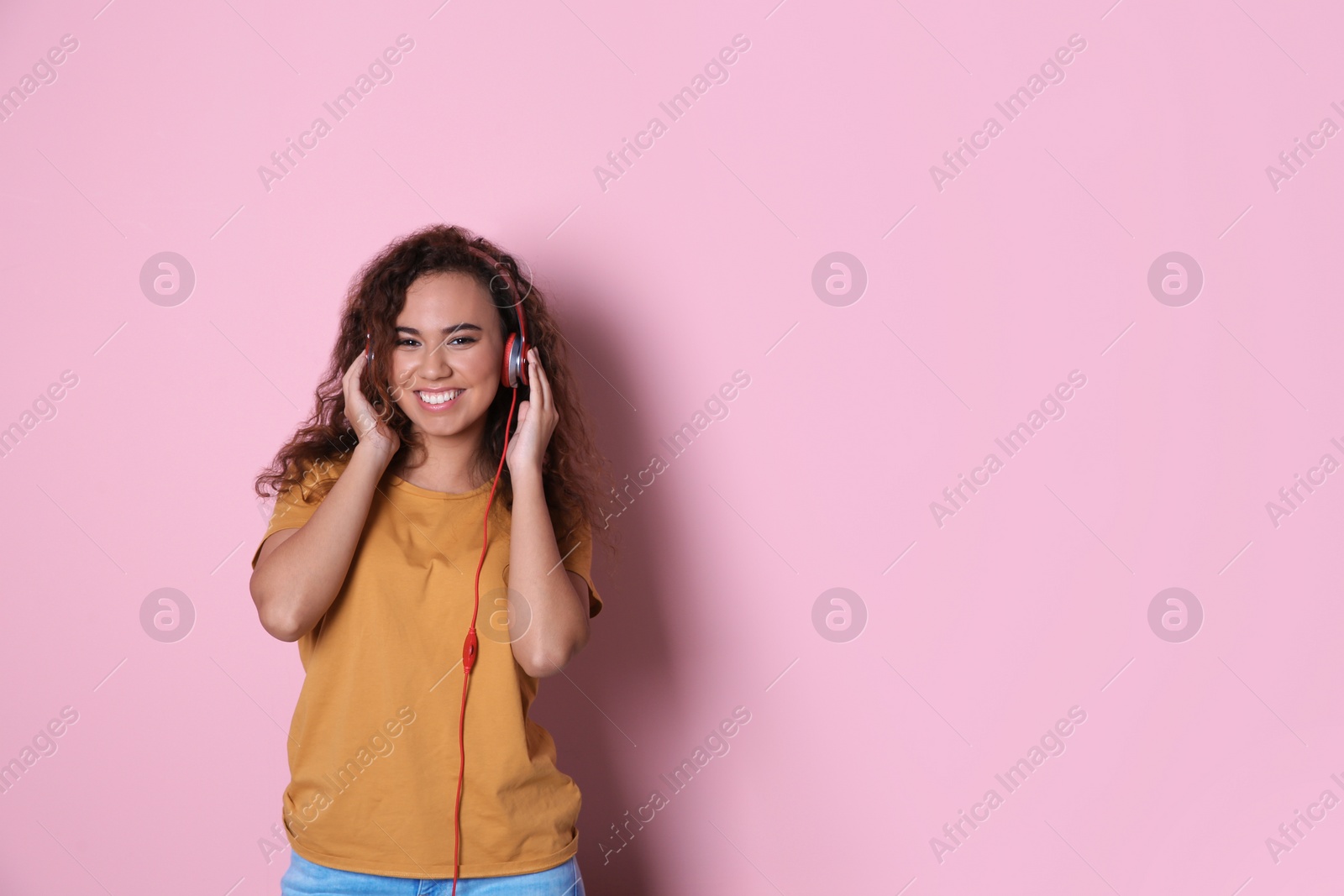 Photo of African-American girl listening to music with headphones on color background, space for text