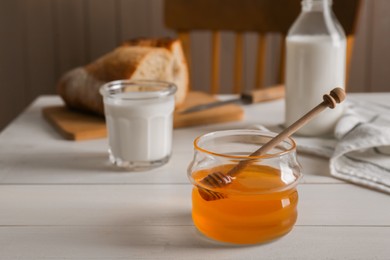 Photo of Jar with honey, milk and bread on white wooden table