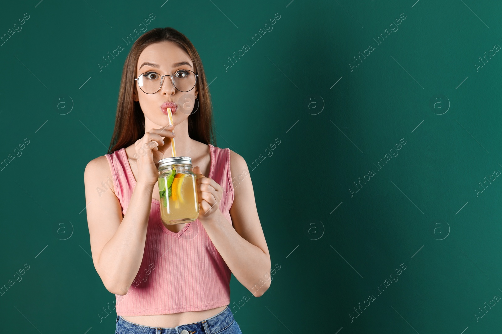 Photo of Emotional young woman drinking natural detox lemonade on green background. Space for text