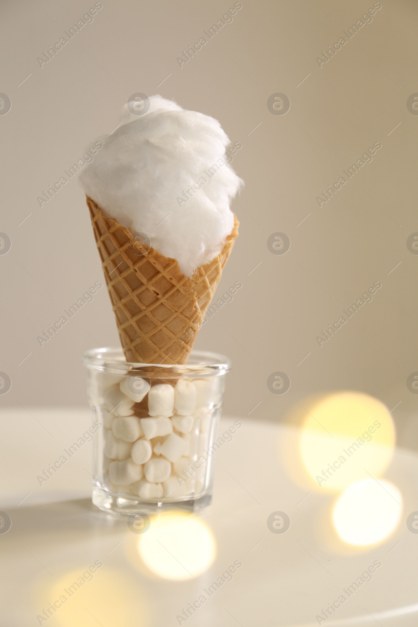 Photo of Sweet cotton candy in waffle cone on table against blurred lights