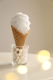 Photo of Sweet cotton candy in waffle cone on table against blurred lights