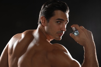 Handsome young man with bottle of perfume on black background