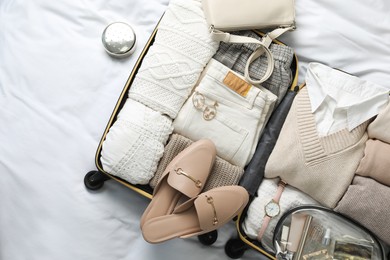 Photo of Open suitcase with folded clothes, shoes and accessories on bed, top view