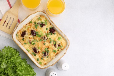 Photo of Tasty sausage casserole with green onions in baking dish served on white table, flat lay. Space for text