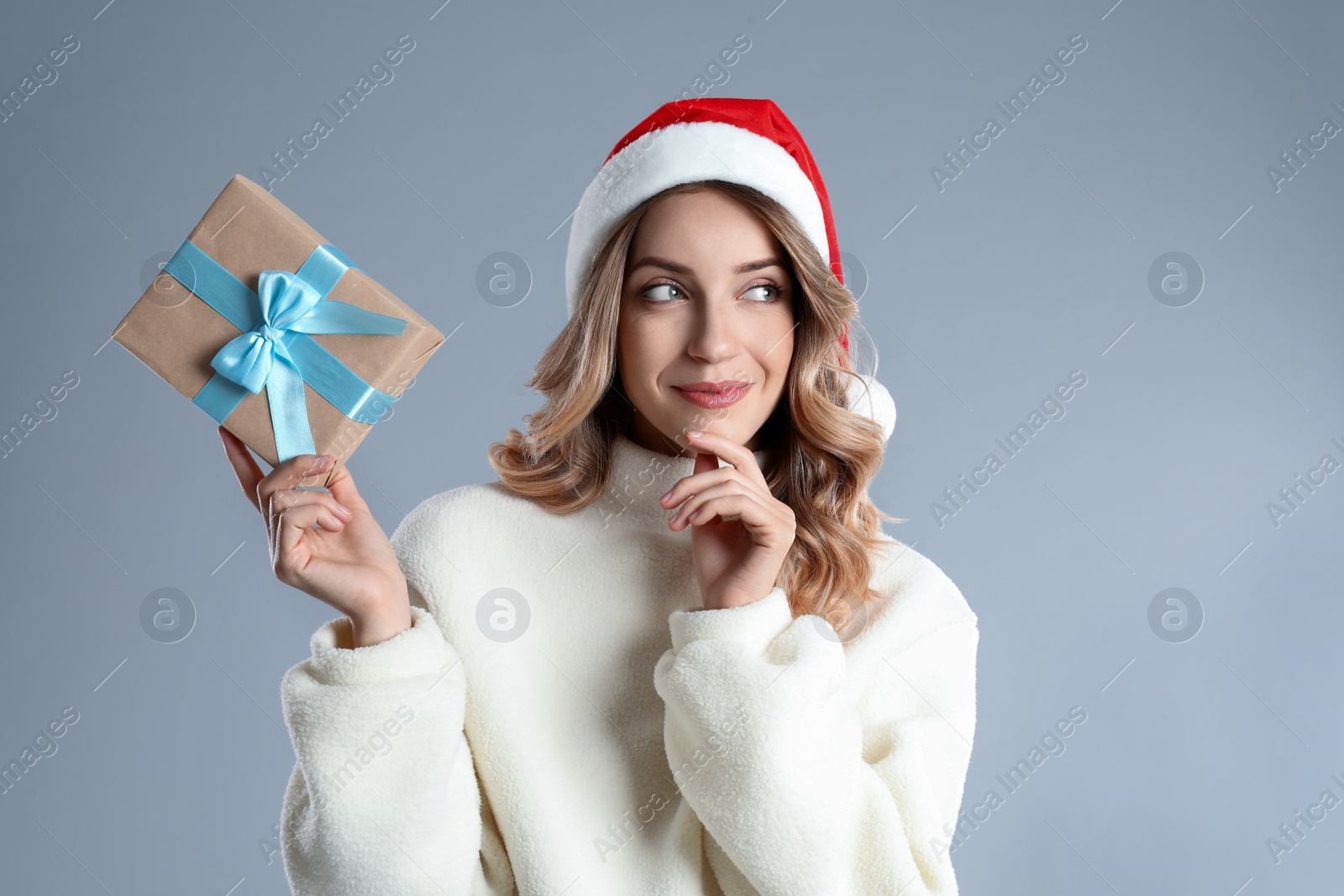 Photo of Beautiful young woman in Santa hat with Christmas present on light grey background