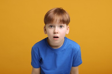 Portrait of surprised little boy on orange background