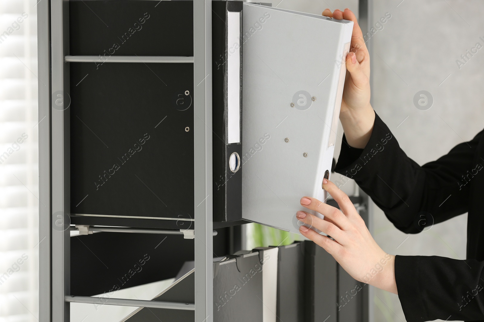 Photo of Woman taking folder with documents from shelf in office, closeup