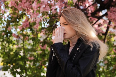 Woman suffering from seasonal pollen allergy near blossoming tree outdoors