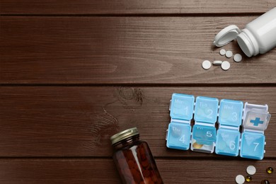 Weekly pill box and bottles with medicaments on wooden table, flat lay. Space for text