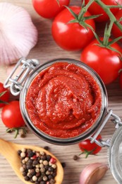 Photo of Jar of tasty tomato paste and ingredients on wooden table, flat lay