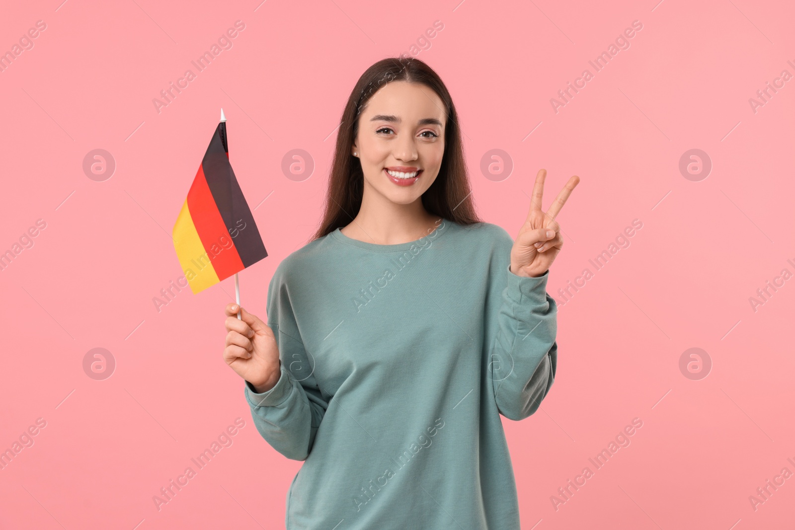 Photo of Young woman holding flag of Germany and showing V-sign on pink background