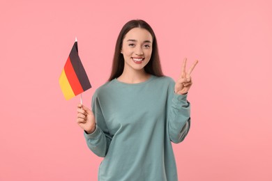 Photo of Young woman holding flag of Germany and showing V-sign on pink background