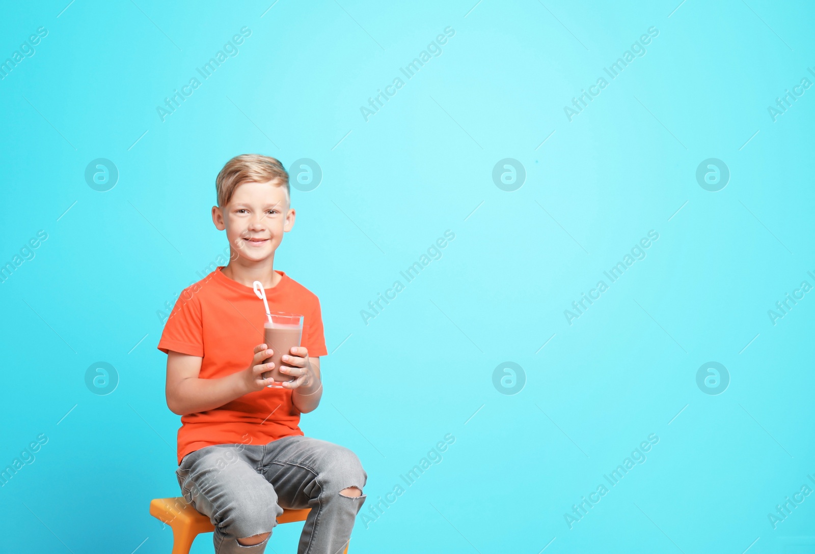 Photo of Little boy with glass of milk shake on stool against color background