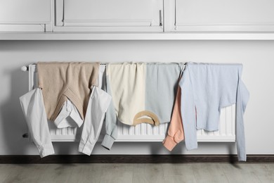 Clean clothes hanging on white radiator in room