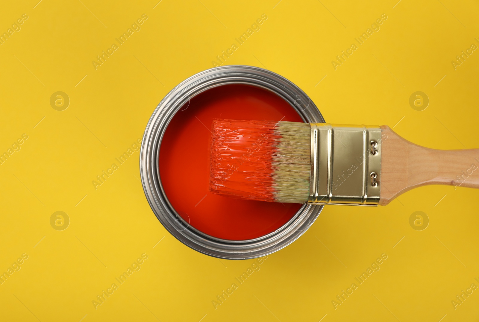 Photo of Can of red paint and brush on yellow background, top view