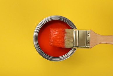 Photo of Can of red paint and brush on yellow background, top view