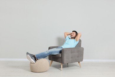 Photo of Happy man sitting in armchair near light gray wall indoors