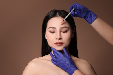 Woman getting facial injection on brown background