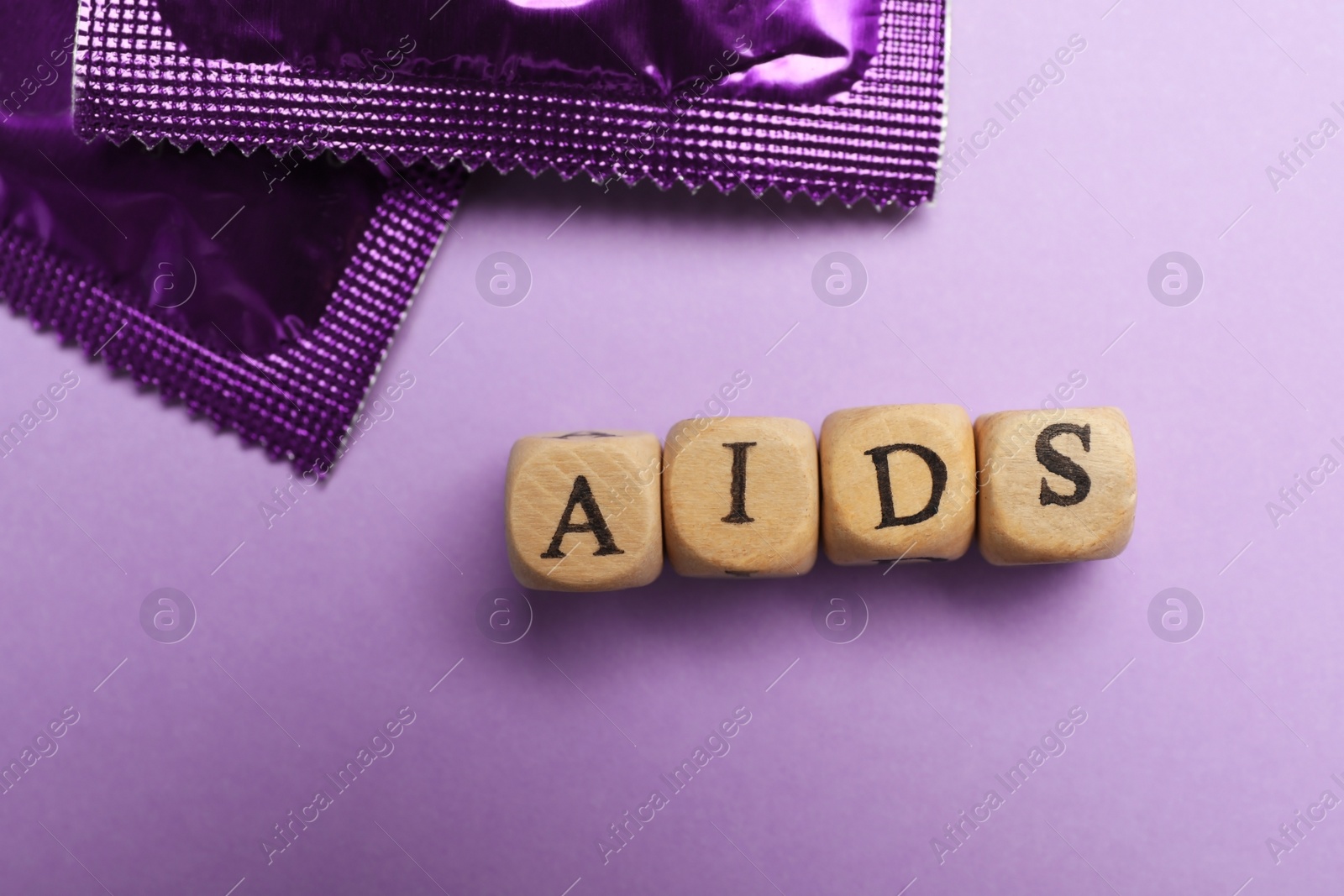 Photo of Condoms and word AIDS made with wooden cubes on violet background, flat lay. Safe sex