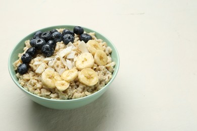 Photo of Tasty oatmeal with banana, blueberries, coconut flakes and honey served in bowl on beige table, space for text