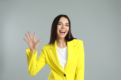 Woman showing number five with her hand on grey background