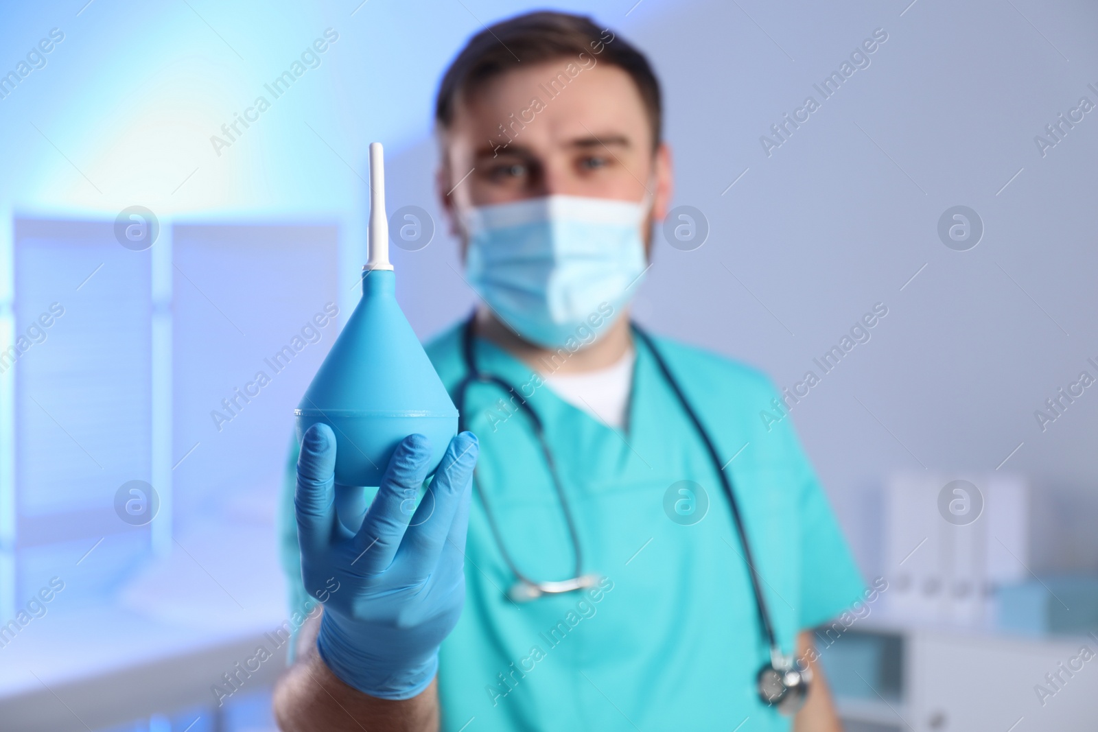 Photo of Doctor holding rubber enema in examination room, focus on hand. Space for text