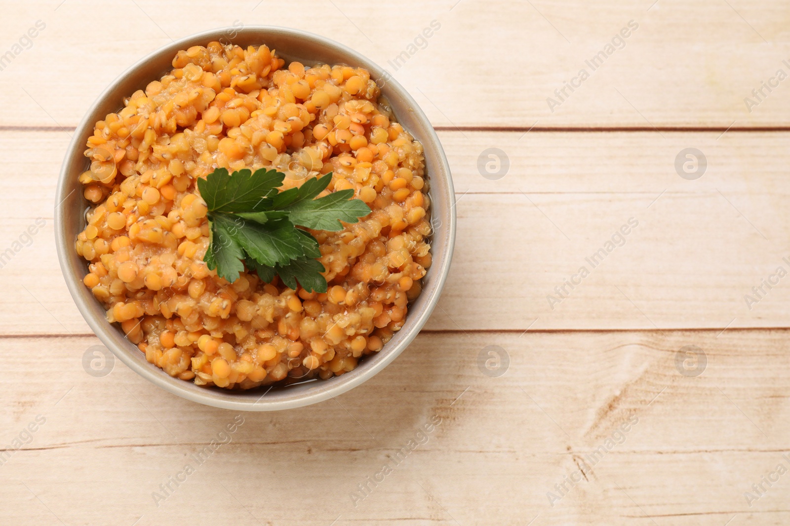 Photo of Delicious red lentils with parsley in bowl on wooden table, top view. Space for text