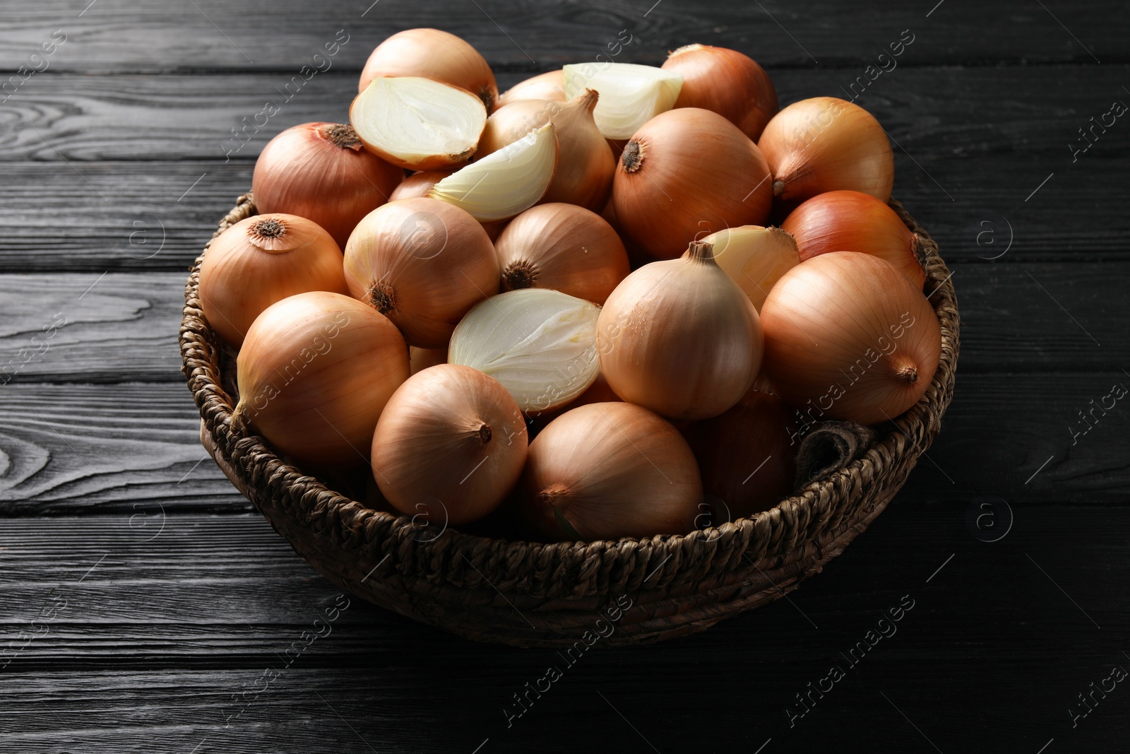 Photo of Whole and cut onions on black wooden table