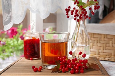 Photo of Helpful viburnum berries and drink on wooden board indoors