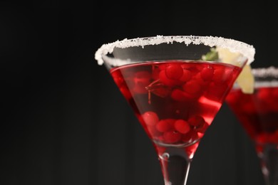 Photo of Tasty cranberry cocktail in glasses against black background, closeup. Space for text