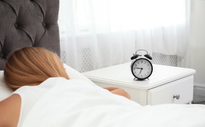 Analog alarm clock and sleepy woman in bedroom. Time of day