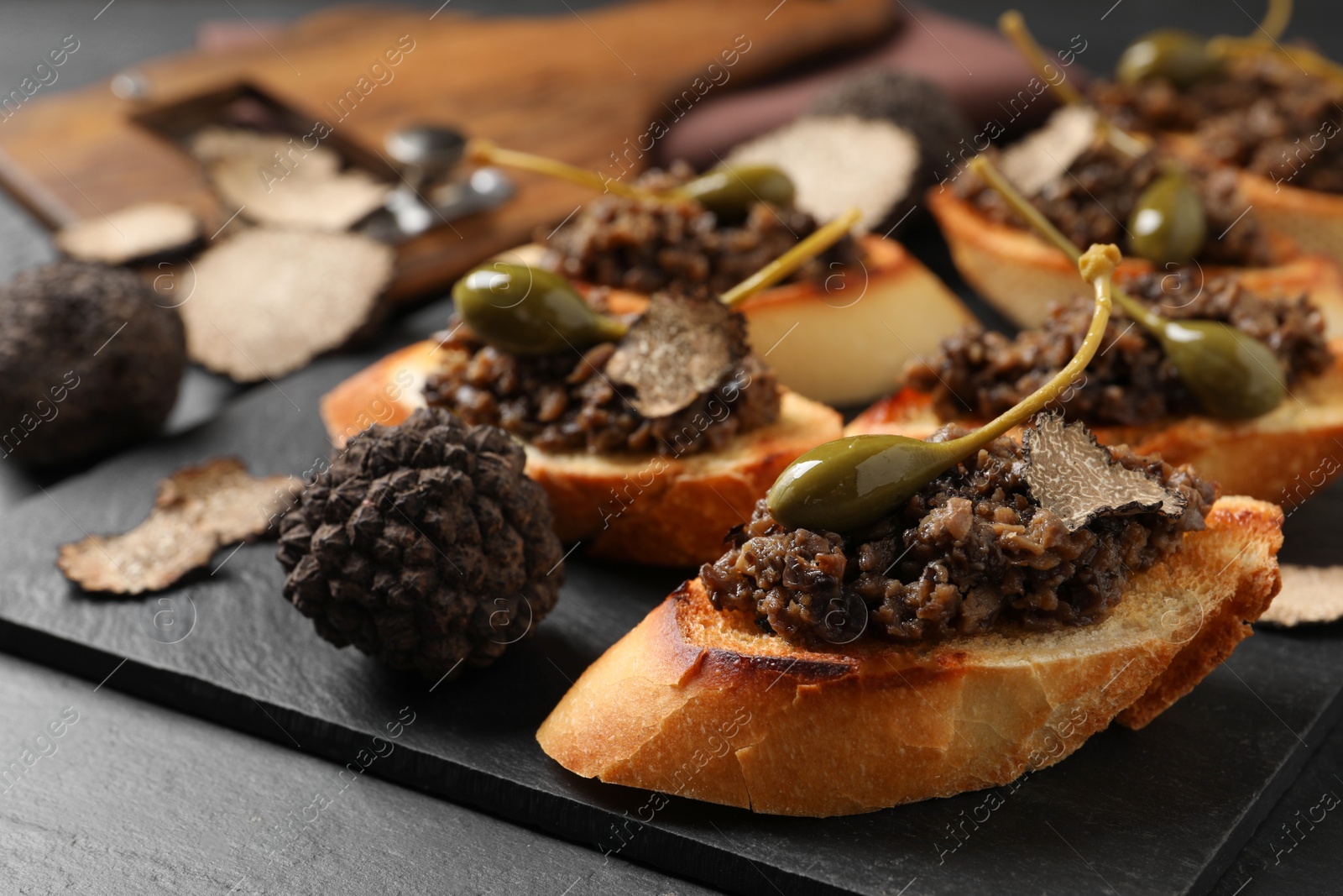 Photo of Tasty bruschettas with truffle paste and capers on black table, closeup