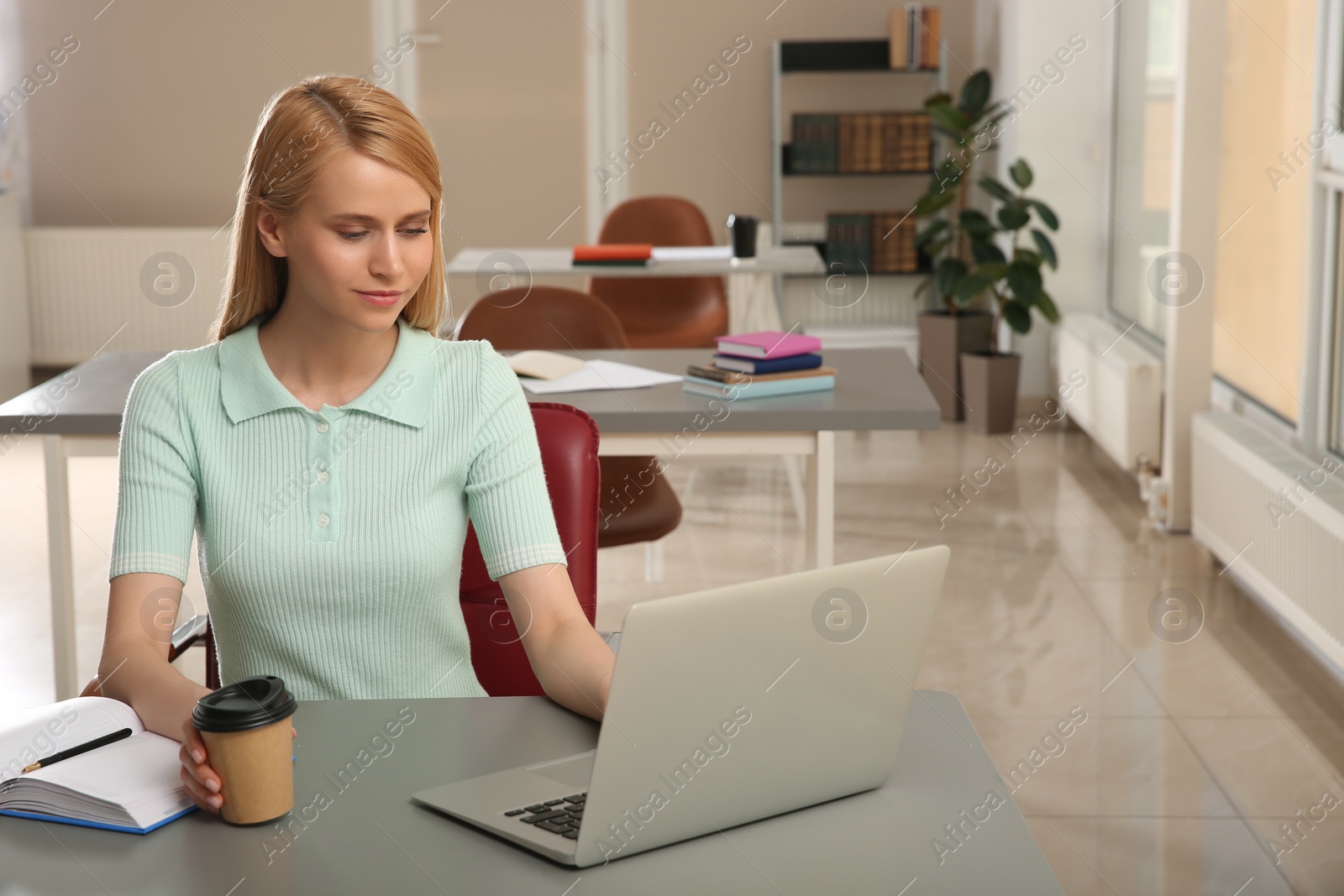 Photo of Young woman with laptop studying at table in library