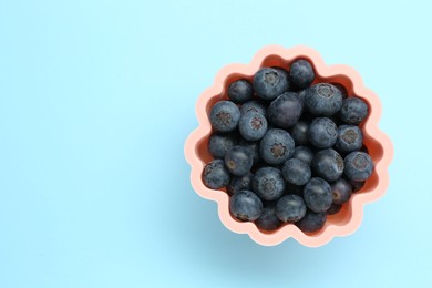 Bowl of fresh delicious blueberries on light blue background, top view. Space for text