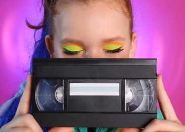 Photo of Cute indie girl with VHS cassette on violet background, closeup