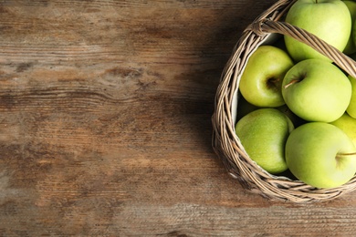 Wicker basket of fresh ripe green apples on wooden table, top view. Space for text