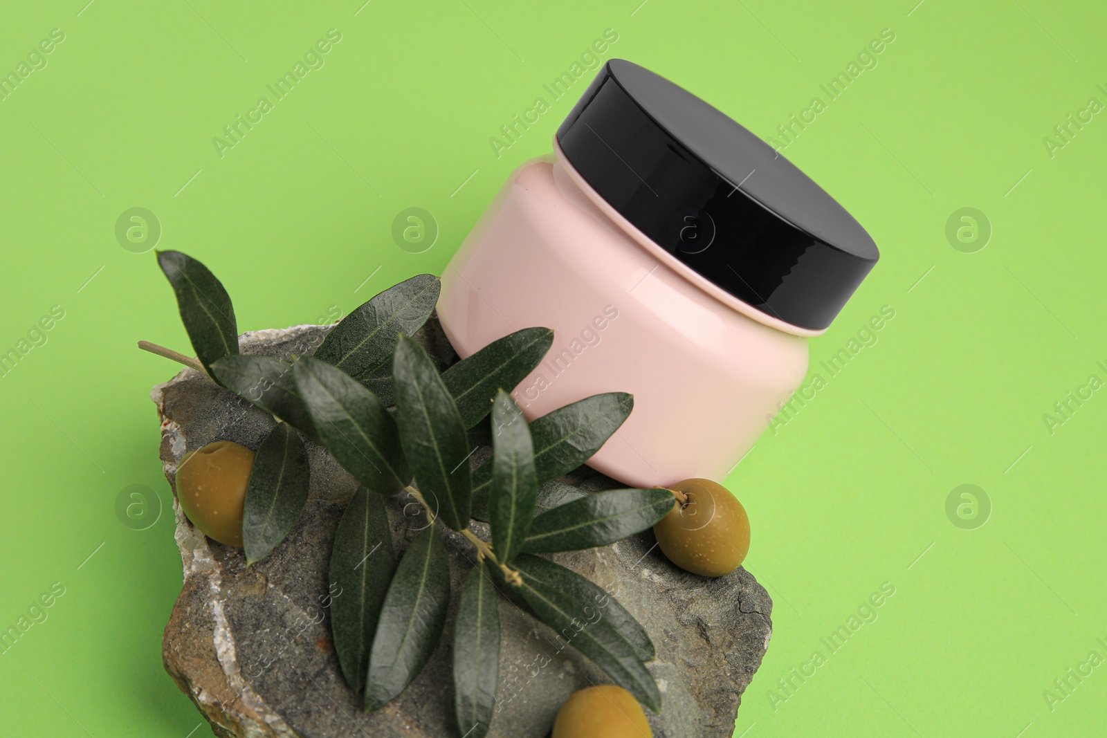 Photo of Jar of cream and olives on light green background, above view