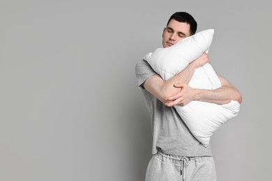 Man in pyjama holding pillow and sleeping on grey background, space for text