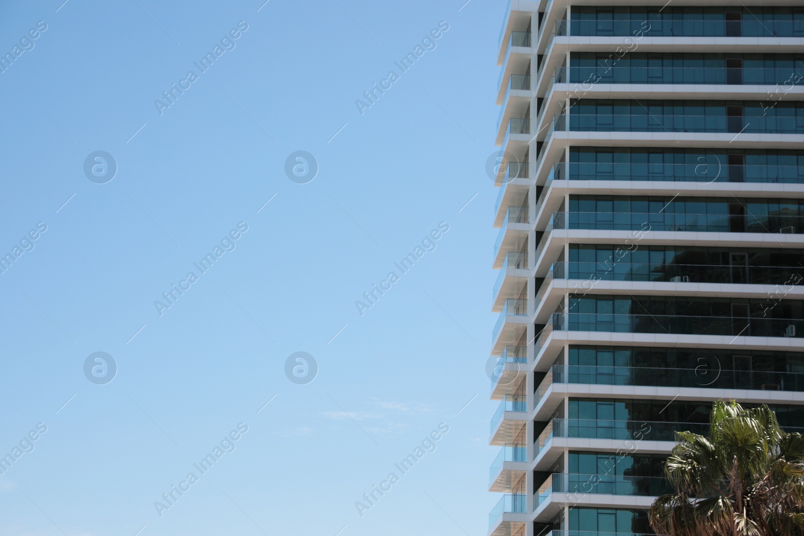 Photo of Exterior of residential building with balconies against blue sky, low angle view. Space for text