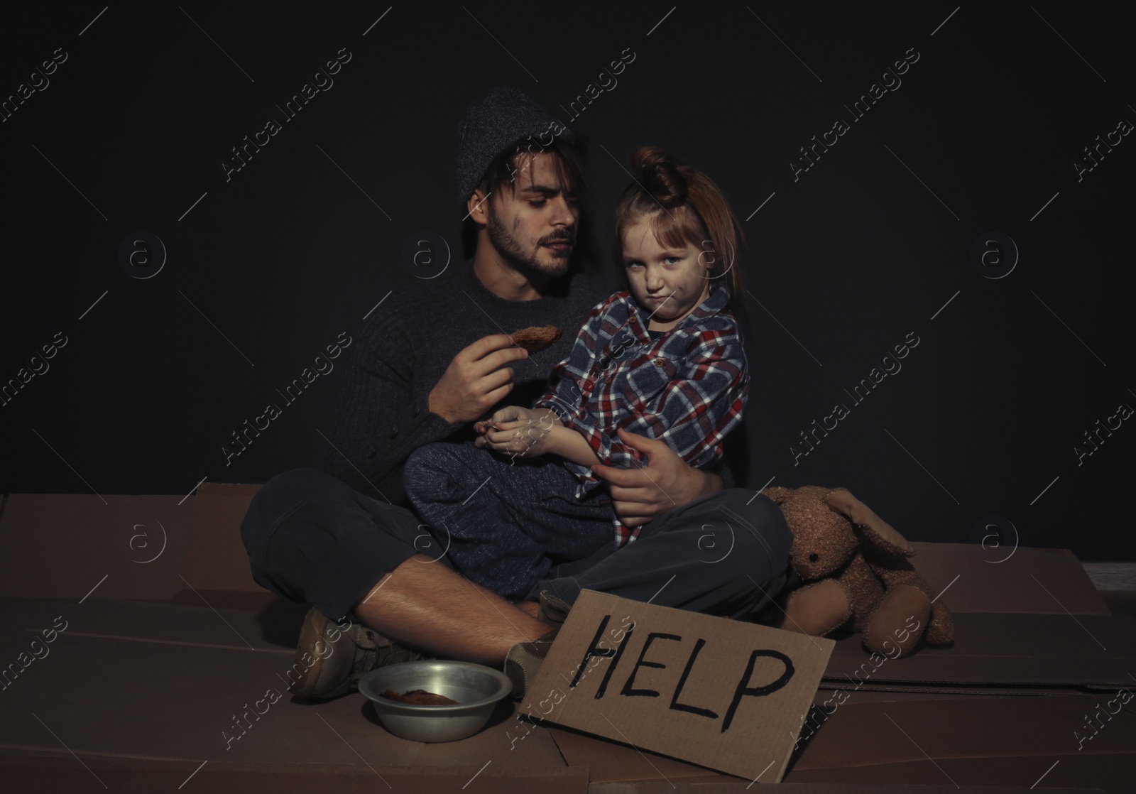 Photo of Poor father and daughter with HELP sign on floor near dark wall