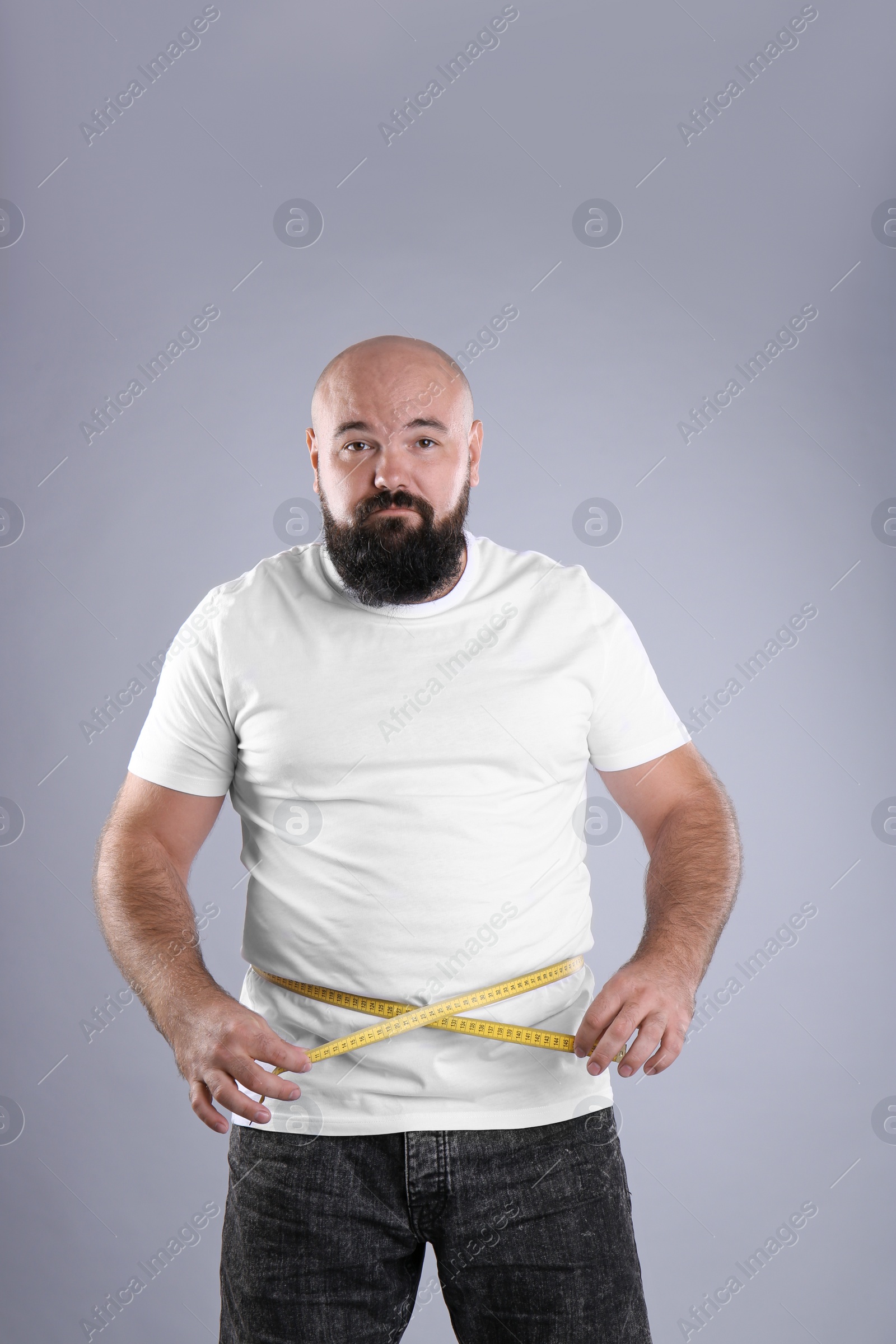 Photo of Fat man with measuring tape on grey background. Weight loss