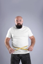 Fat man with measuring tape on grey background. Weight loss