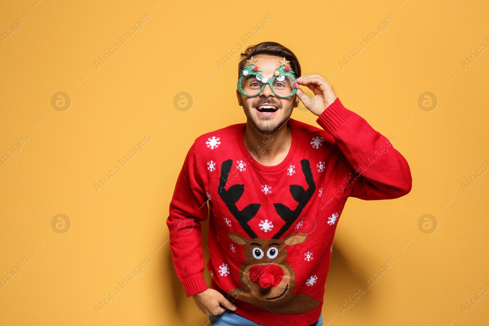 Photo of Young man in Christmas sweater with party glasses on color background