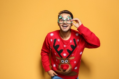 Photo of Young man in Christmas sweater with party glasses on color background