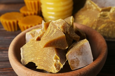 Bowl with natural beeswax blocks on wooden table, closeup