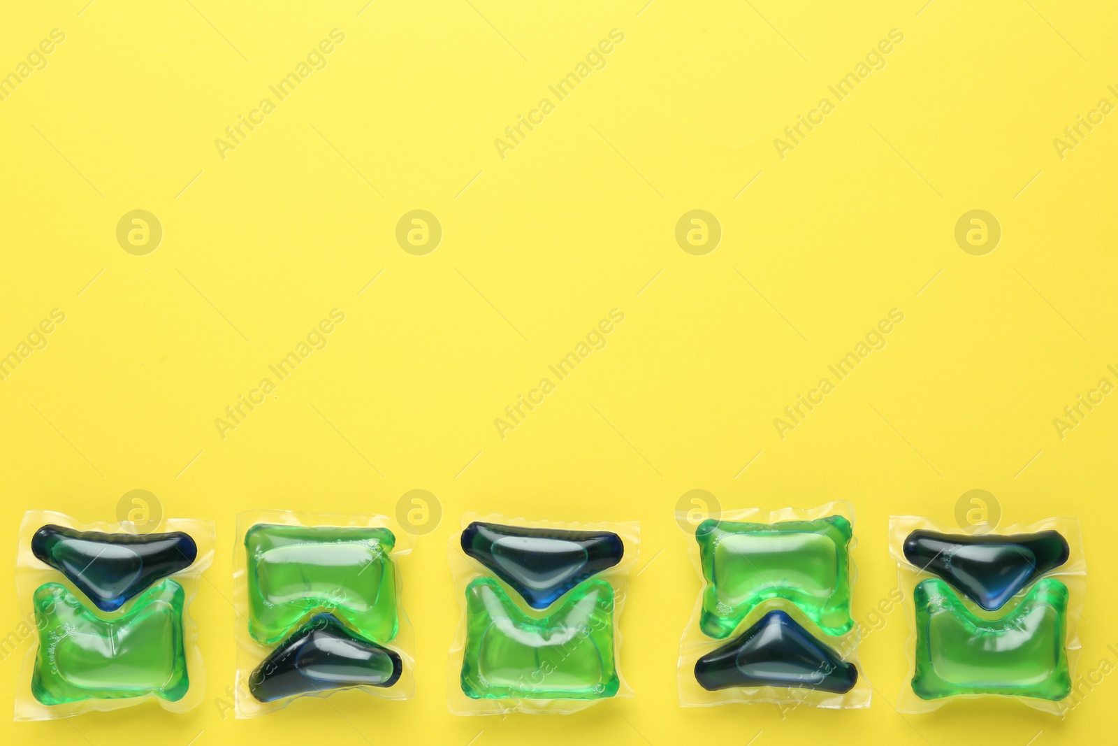 Photo of Laundry capsules on yellow background, flat lay. Space for text