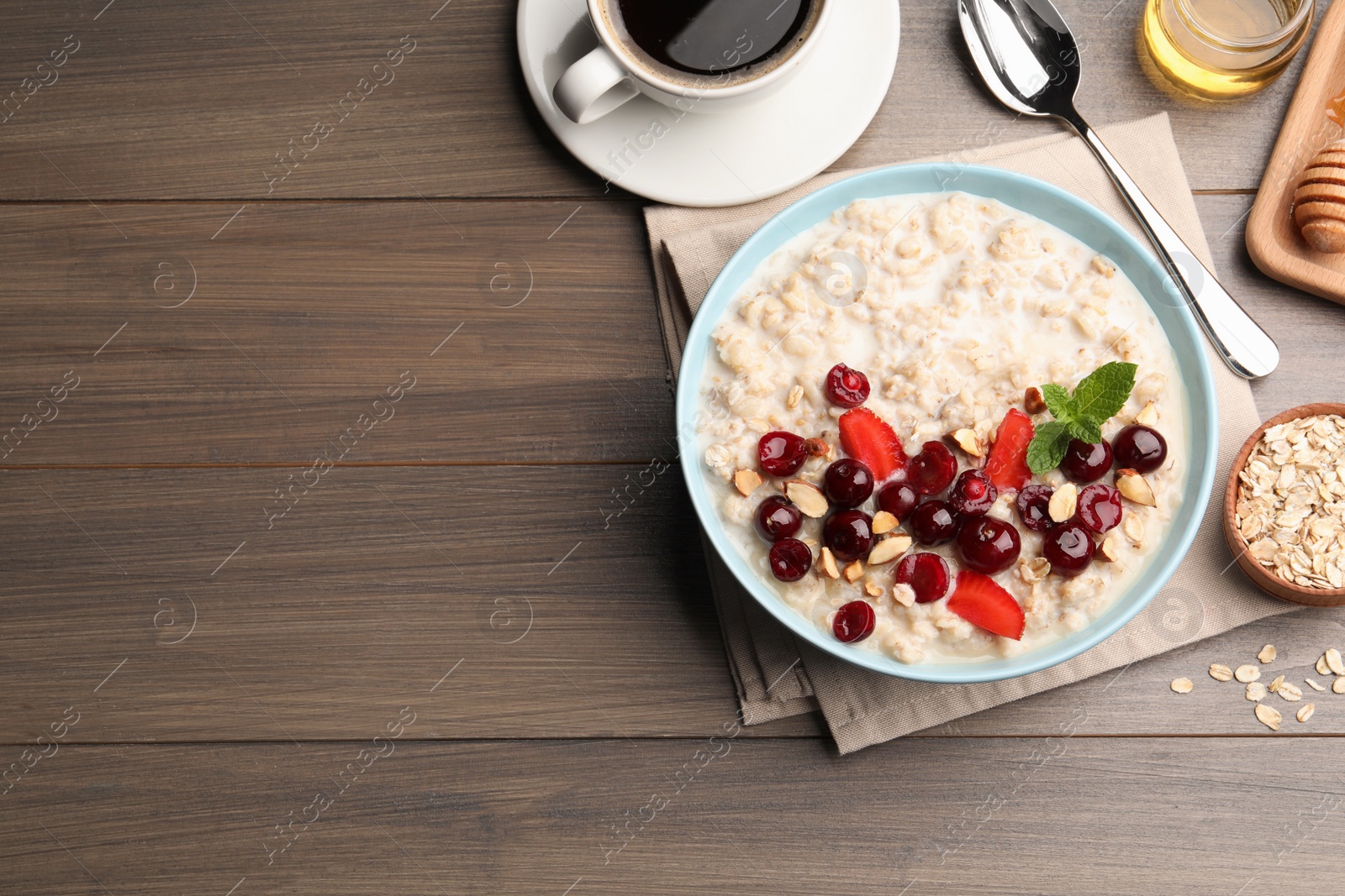 Photo of Bowl of oatmeal porridge served with berries on wooden table, flat lay. Space for text